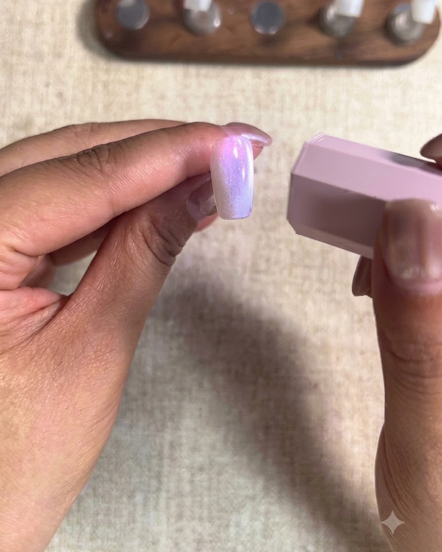 A close-up view of a brush applying a peach nude gel polish onto an index fingernail.