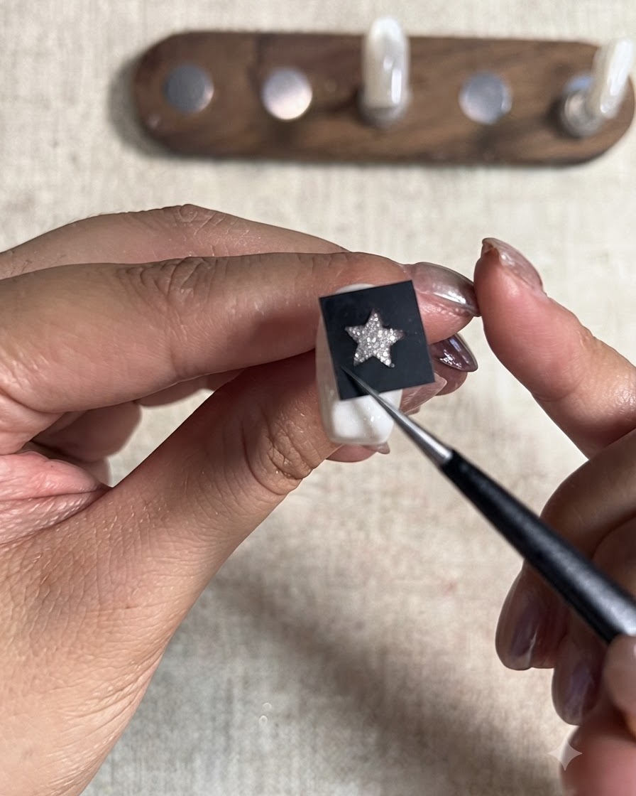 A pointed tool pressing down firmly on a black star stencil sticker placed over a painted nail tip.