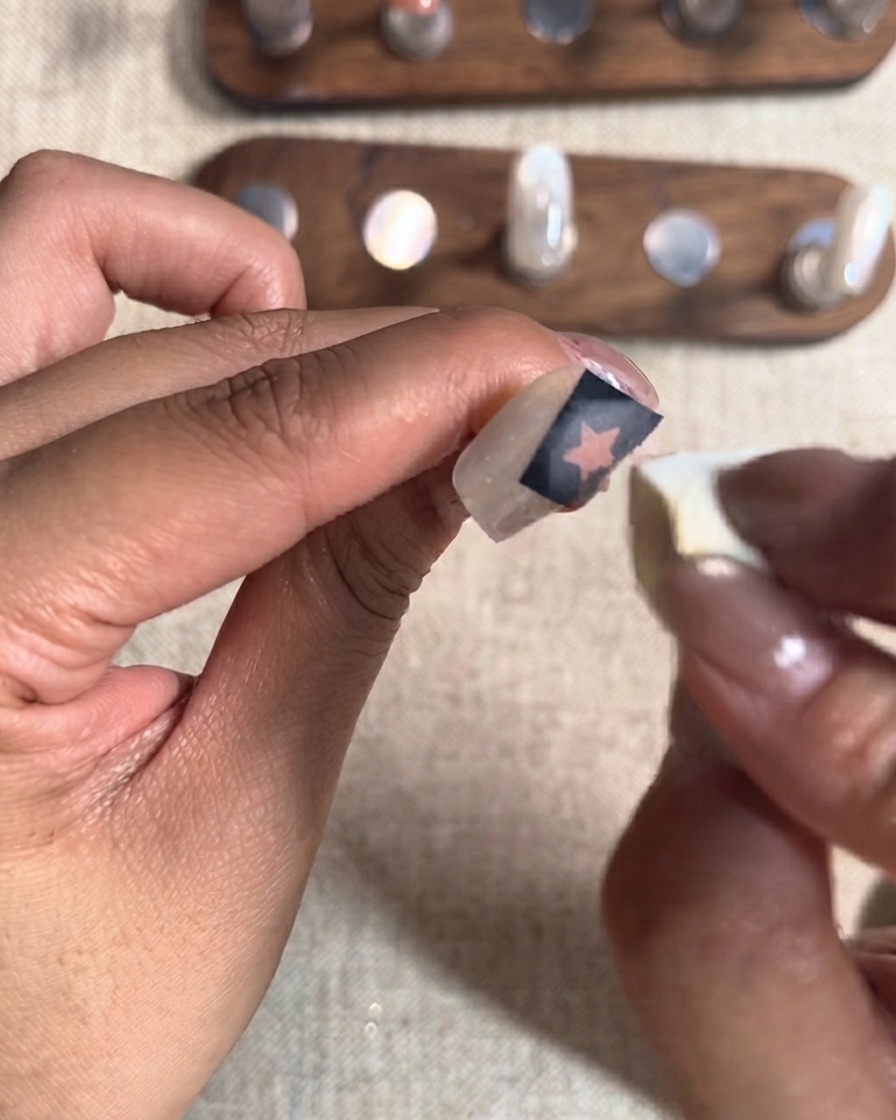A small cosmetic sponge dabbing a second layer of red gel over a star cutout sticker on a fingernail.