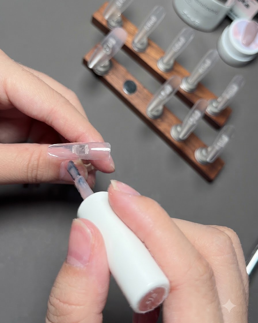 A brush applying nude color gel to the ring finger nail.