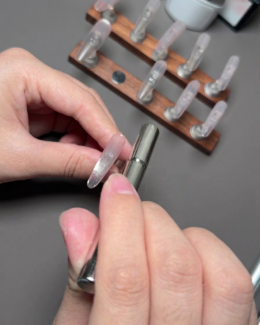 A magnetic wand hovering near a nail to gather and shape the reflective cat eye particles.