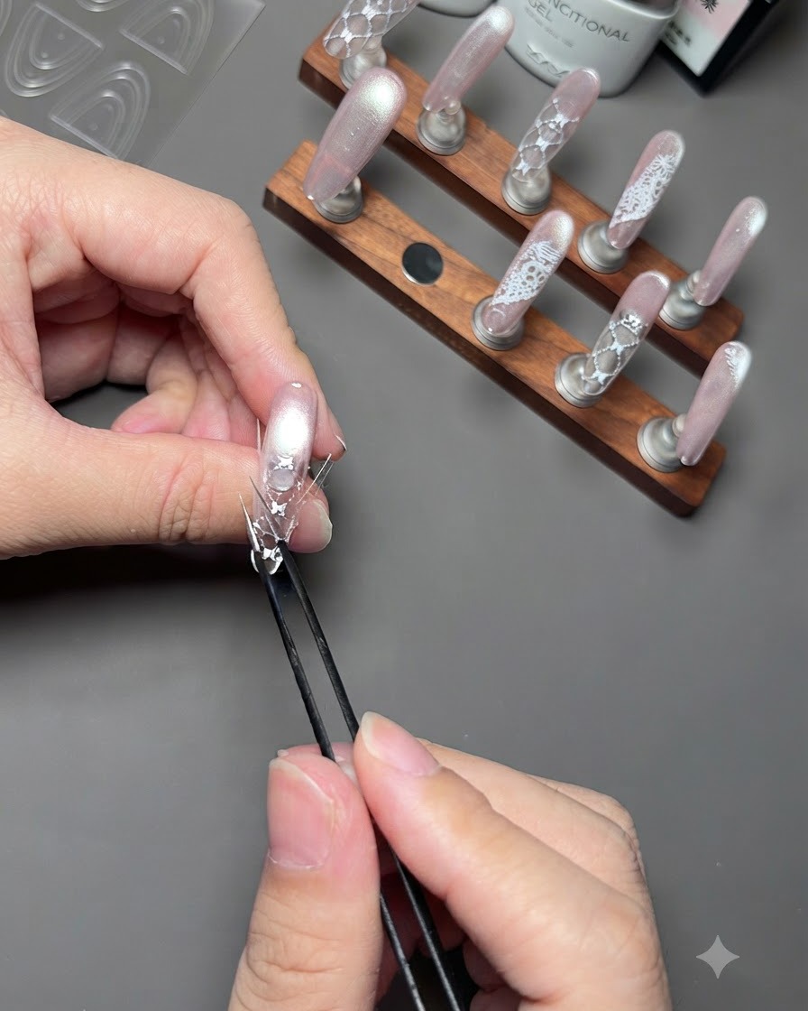 A pair of tweezers pressing down the edges of a curved sticker onto a decorated nail on a display stand.