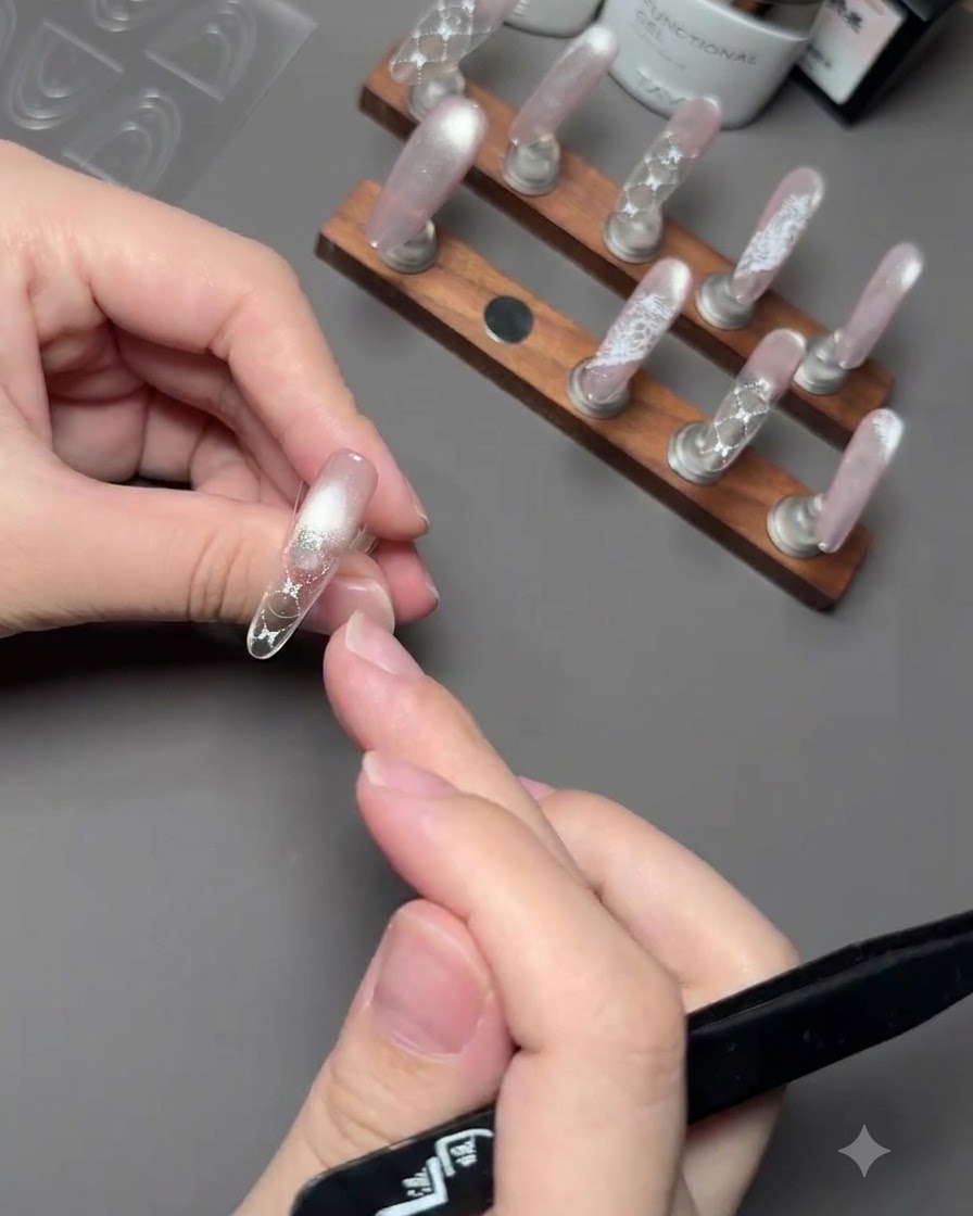 A hand holding a brush to apply pink gel polish onto the tip of a nail above a guide sticker.