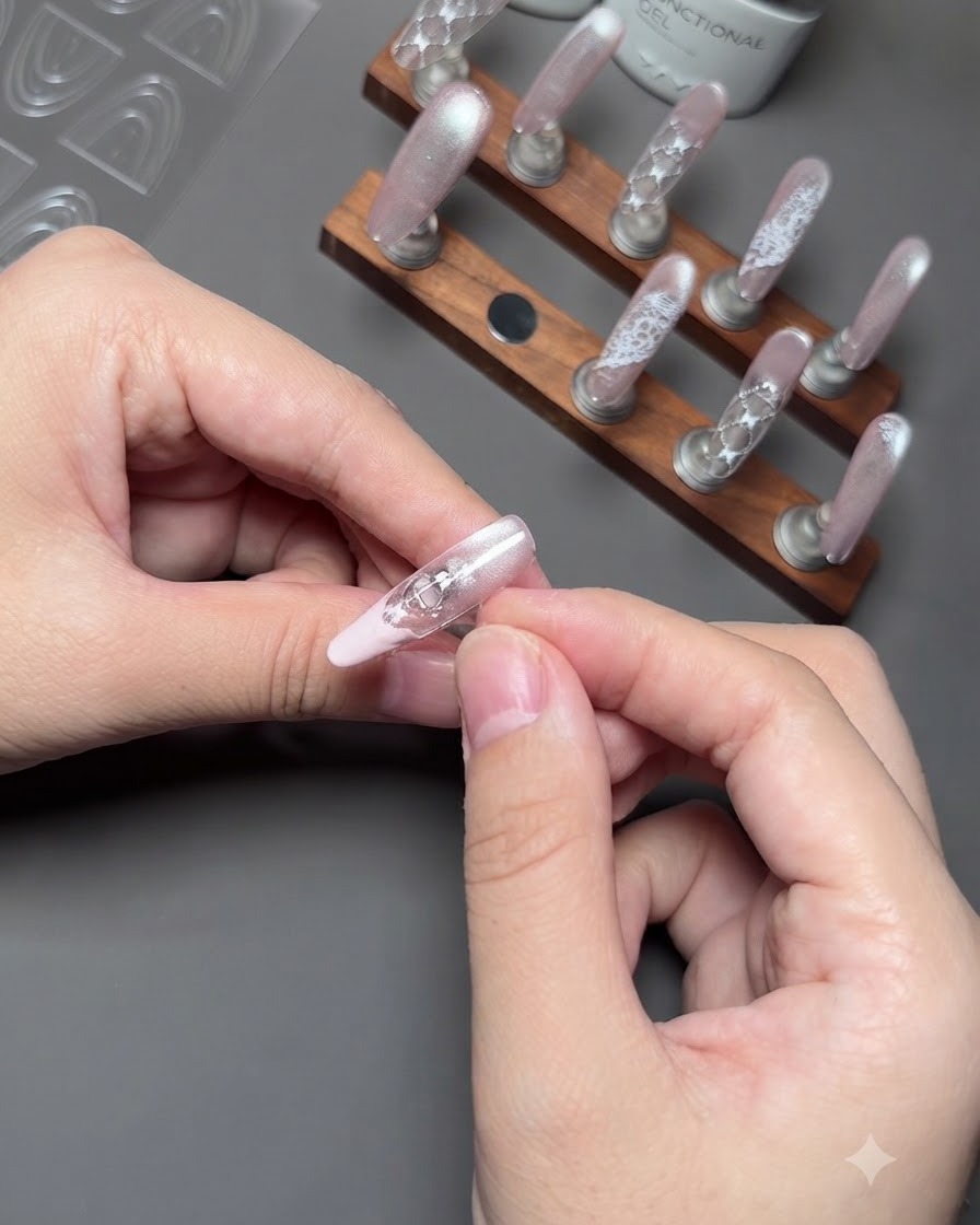 A close-up of fingers gently removing a guide sticker from a nail to expose a neat pink French tip.
