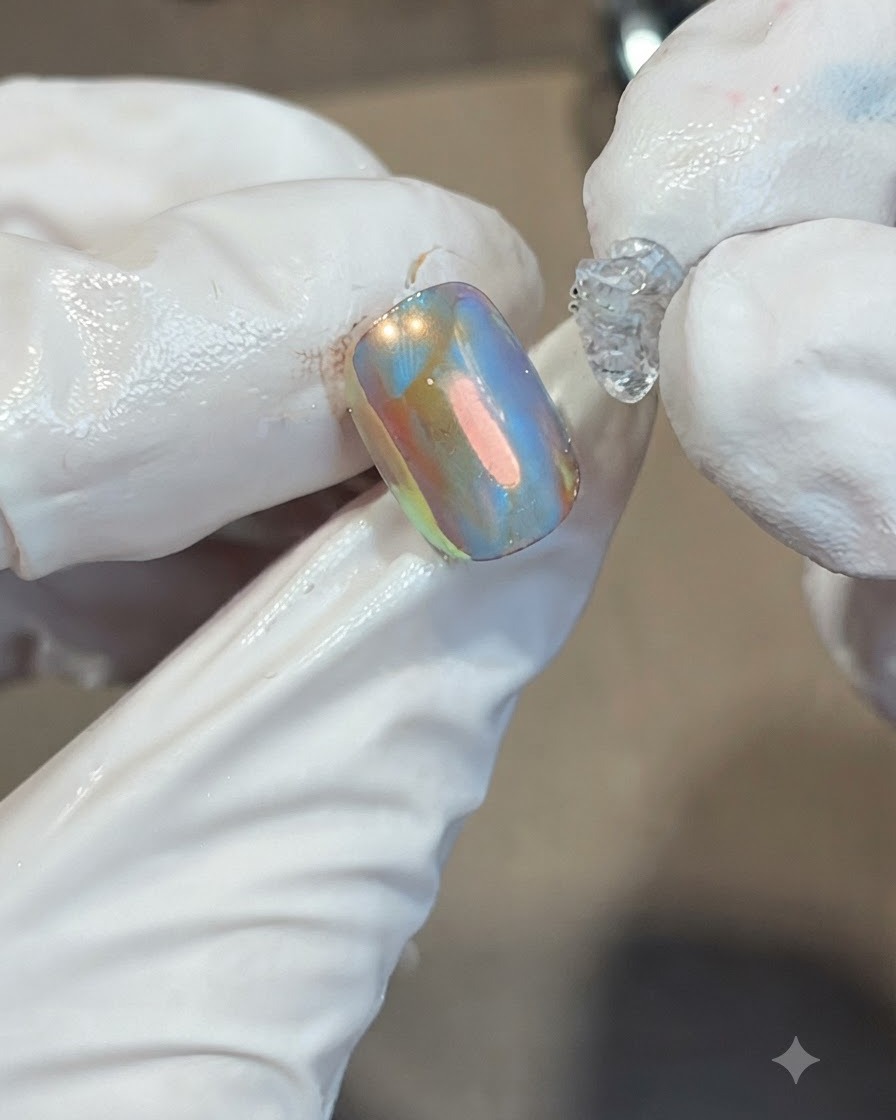 Placing a dollop of thick, clear soft candy gel onto the center of an iridescent orange and blue nail.