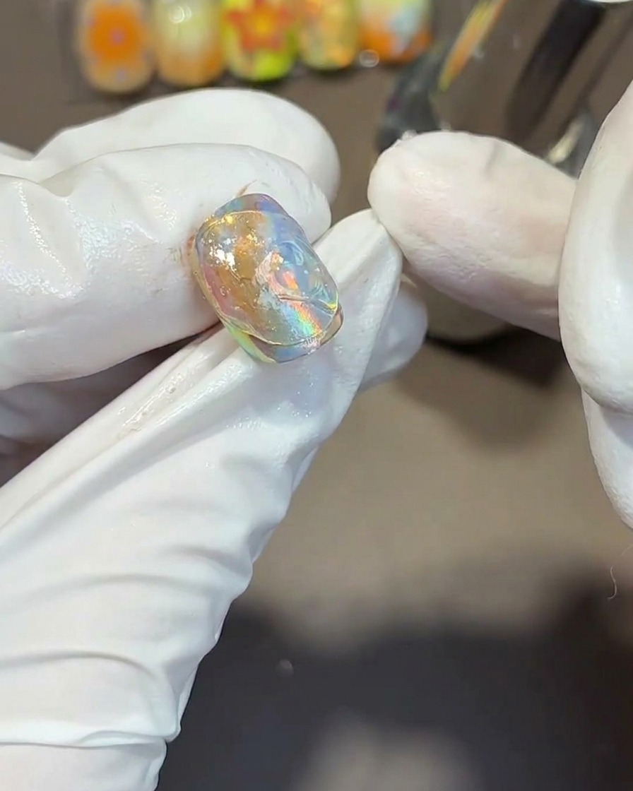 Using a metal tool to press fluid, wavy textures into thick clear gel on top of an iridescent nail tip.