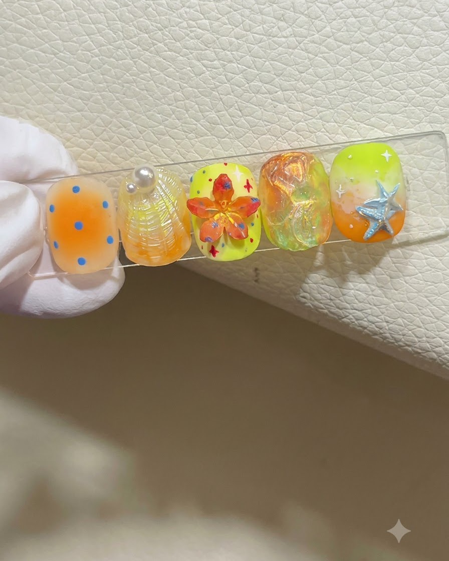 A gloved hand holding a nail display stand showing five colorful summer-themed nail designs.