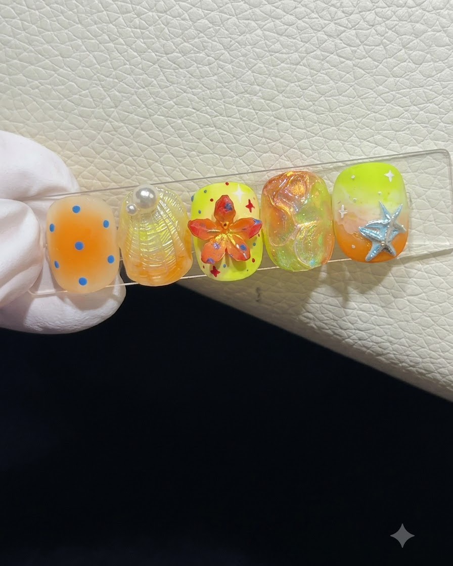 A close-up of a nail display stand showcasing five summer-themed press-on nails with various 3D textures and art.