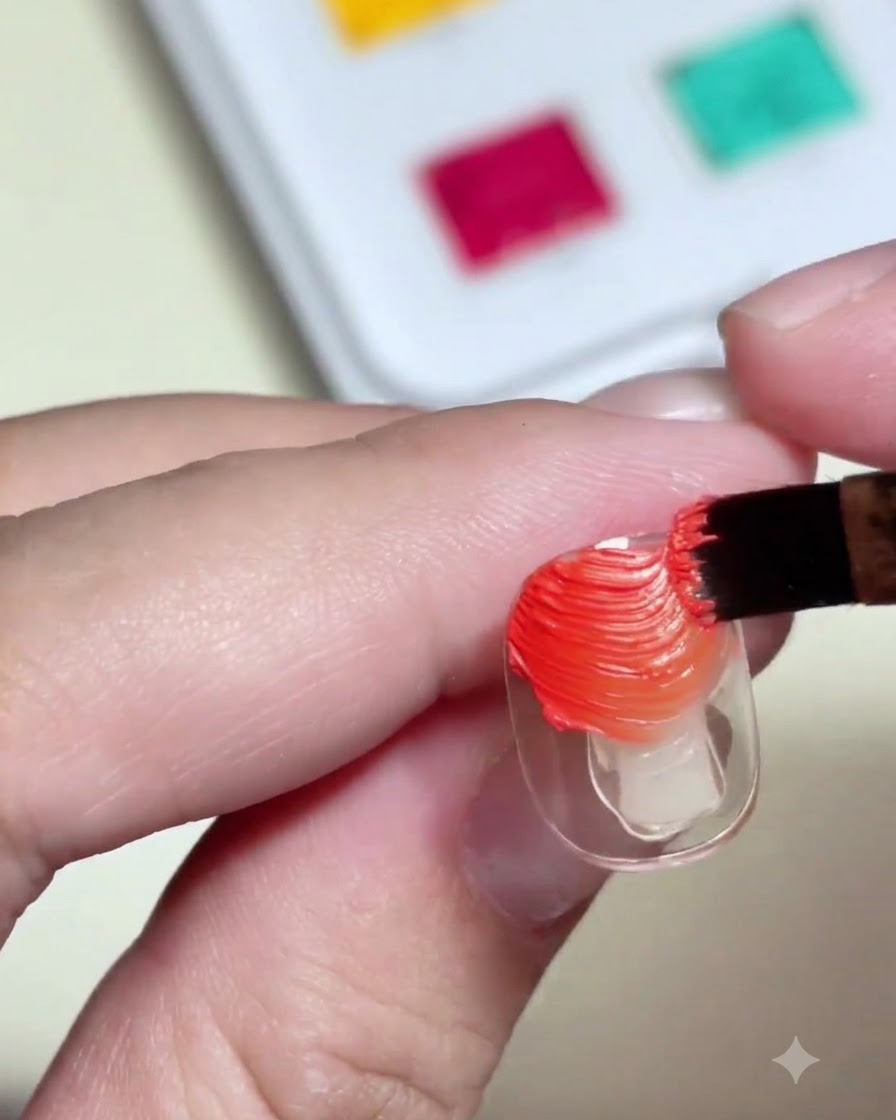 A nail brush applying textured orange and yellow color painting gel onto a clear nail tip.