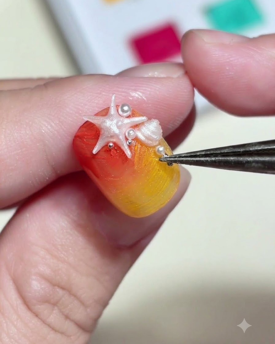 A pair of tweezers placing tiny white pearl beads and metallic studs around a 3D starfish charm on a nail.