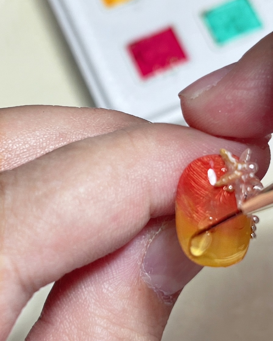 A brush drawing a raised glossy water ripple line with a hard top coat over a textured orange and yellow gradient nail.