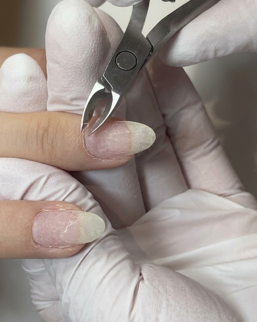 Metal cuticle nippers carefully trimming excess skin around the nail fold of a prepped finger.