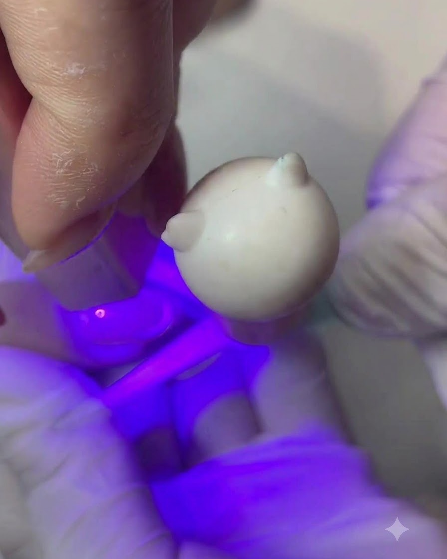 A fine brush applying a thin layer of nude peach color gel onto a fingernail.