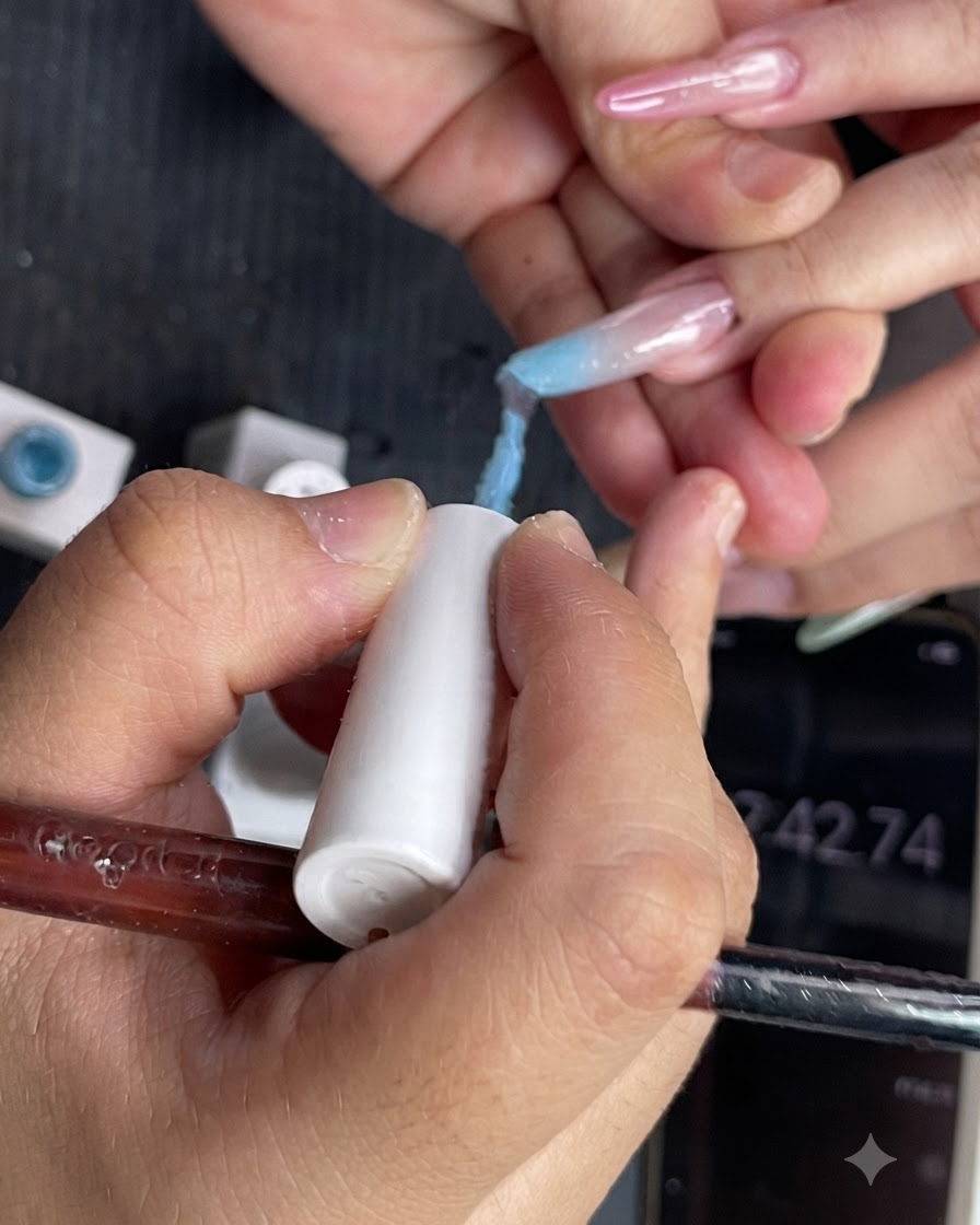 A close-up view of light blue gel polish being applied to the upper half of a fingernail.