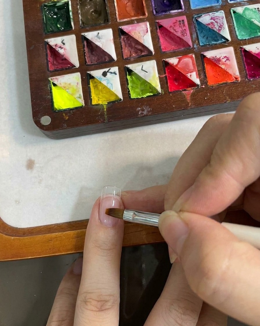 A flat brush tool blending the gradient color on the nail surface.