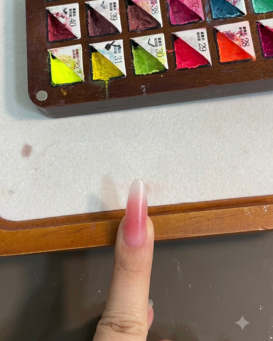 A fingernail with a pink blush gradient under a UV lamp for curing.