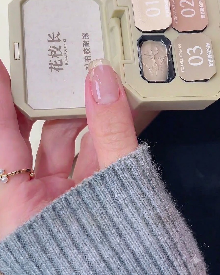 A close-up of a natural fingernail with a white base coat being applied near the free edge.