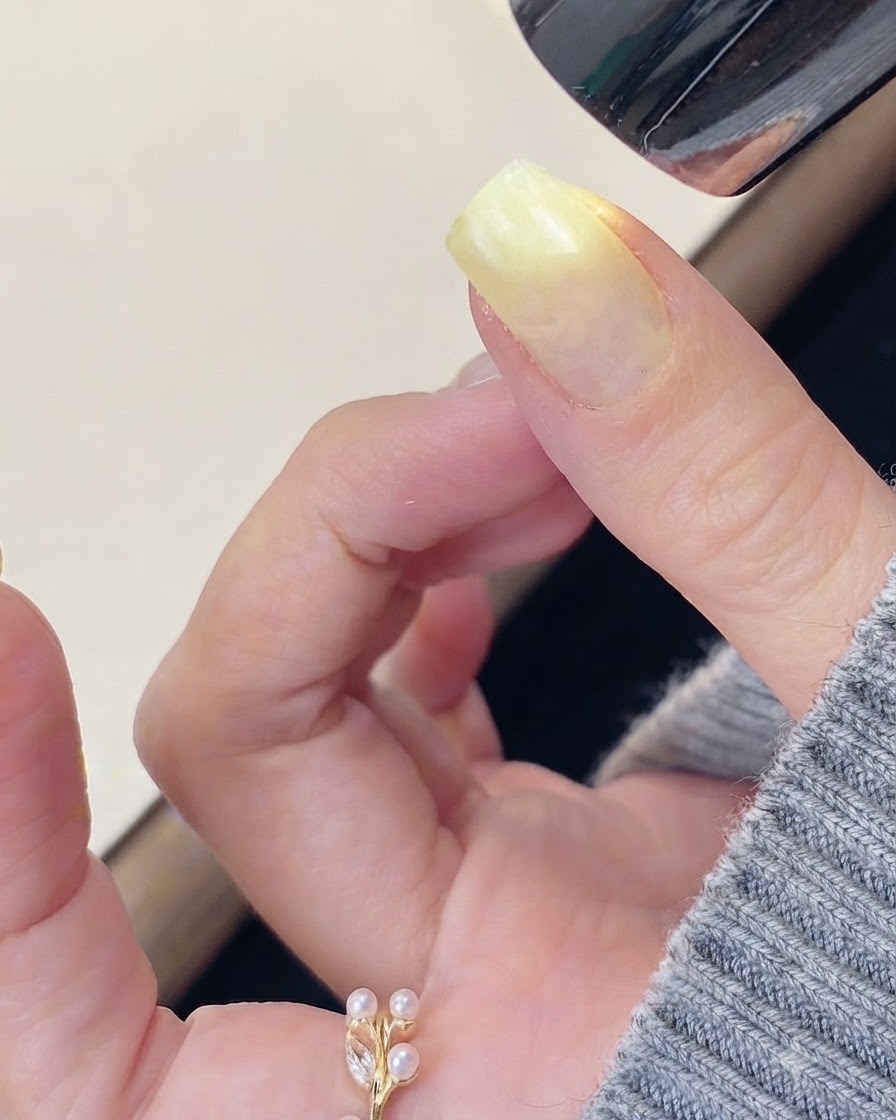 A brush applying clear reinforcing builder gel onto the surface of a prepped fingernail.