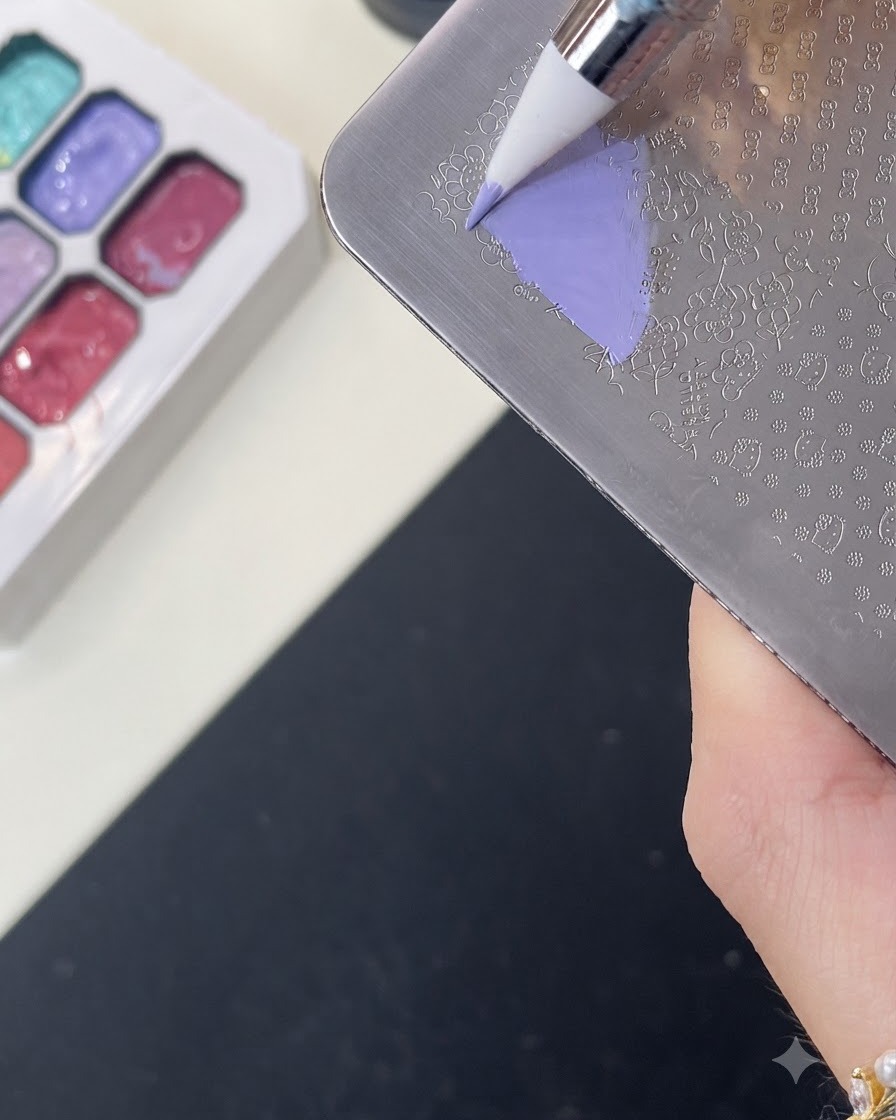 A brush applying purple color gel over a Hello Kitty engraved pattern on a metal stamping plate.