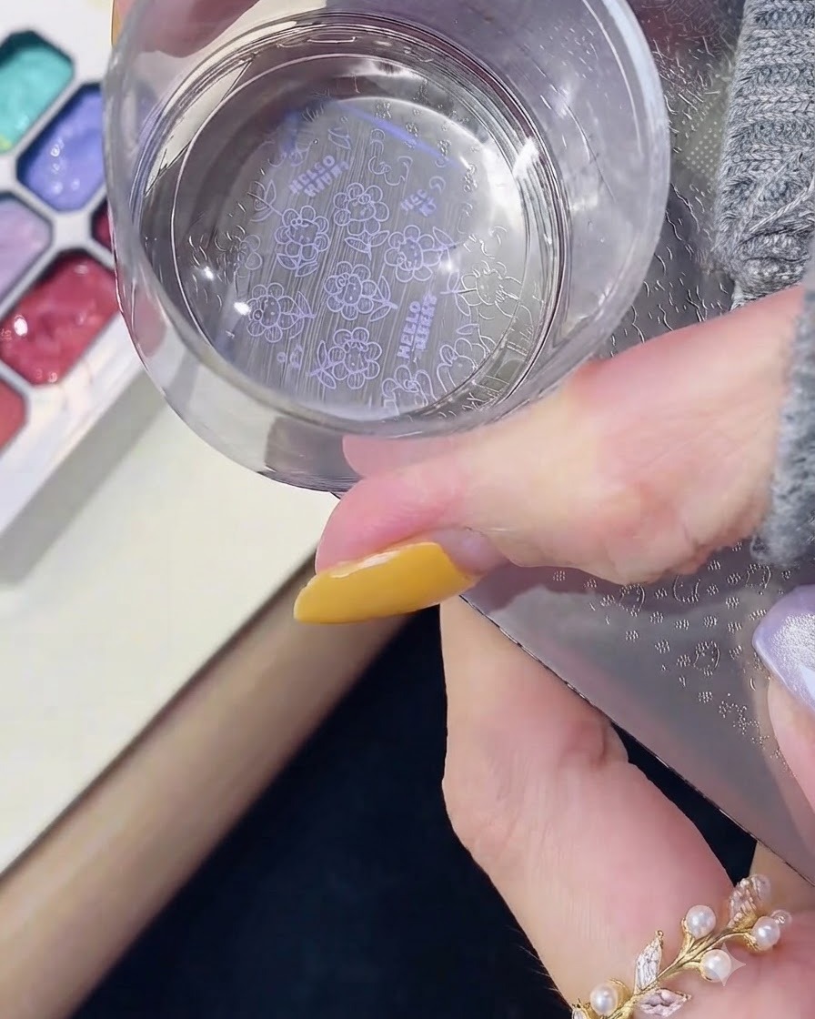 A clear silicone stamper pressing down onto a metal stamping plate to pick up a purple Hello Kitty pattern.