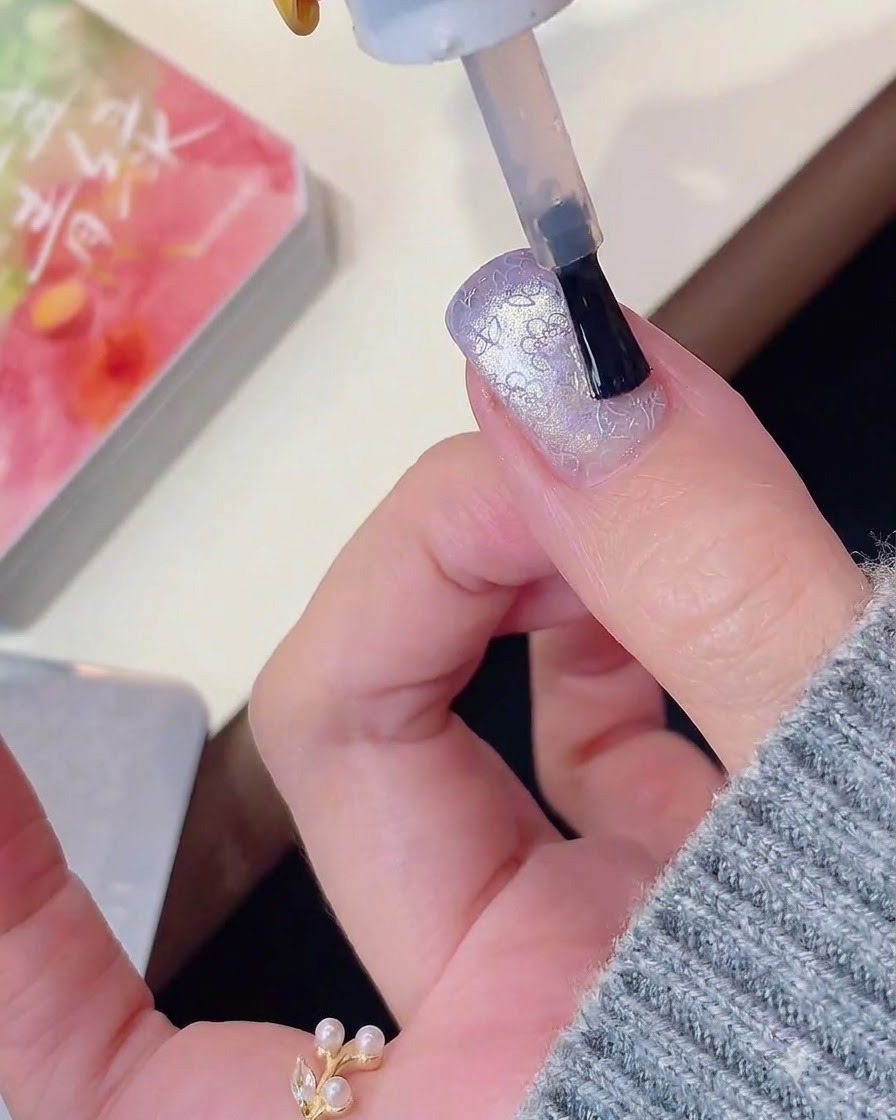 A nail brush applying top coat over a purple cat eye and stamped nail design.