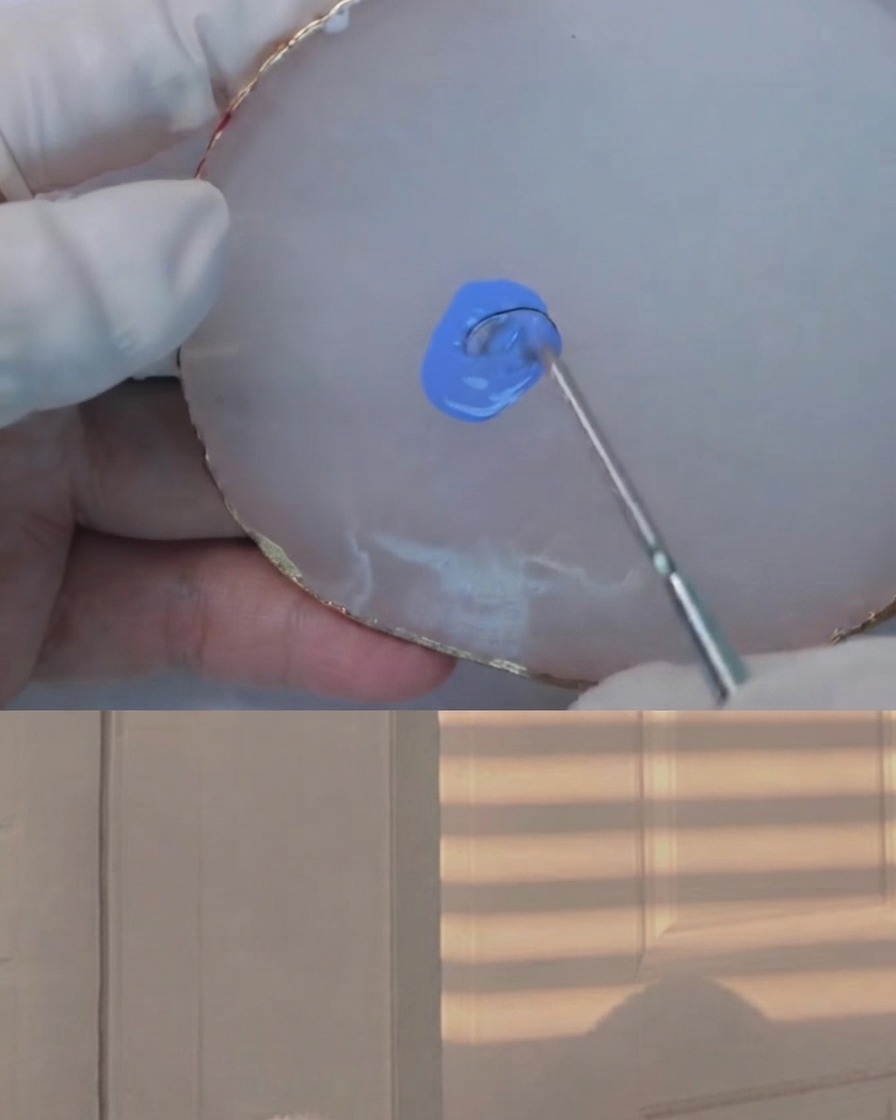 A mixing tool blending a tiny amount of dark gel into a light blue mixture on a white agate palette.