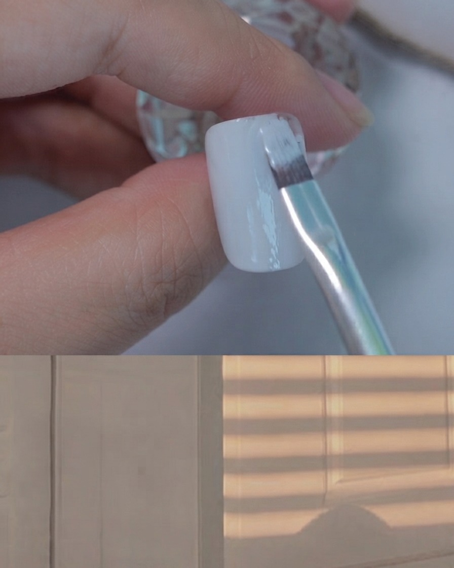 A flat gel brush applying a smooth coat of light grey gel polish onto a display nail.