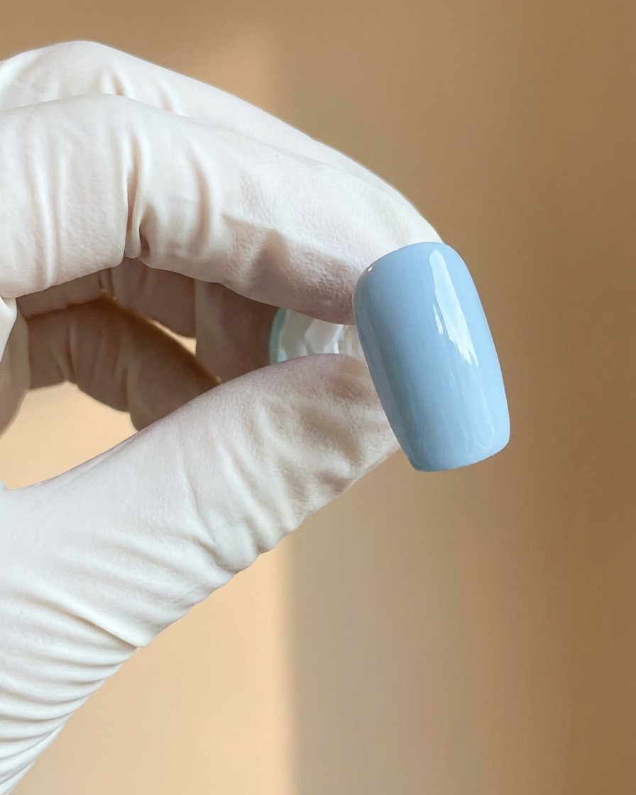 A gloved hand holding a light blue nail with a smooth matte finish.