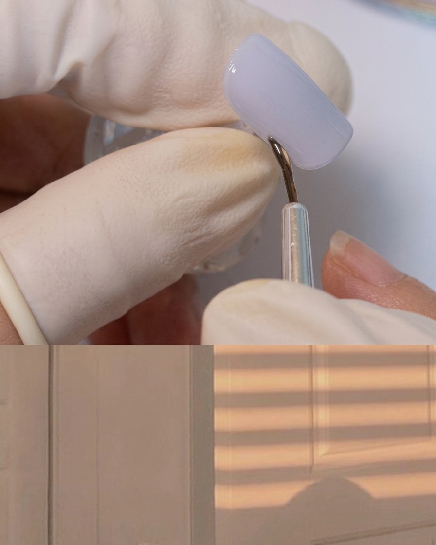 A fine liner brush applying thick adhesive gel around the border of a matte grey nail.