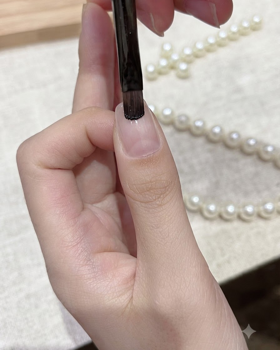 A flat gel brush applying black gel polish onto the free edge of a natural fingernail.