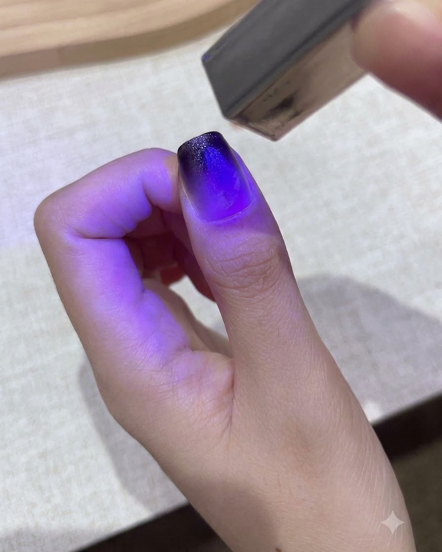 A small purple handheld UV/LED lamp curing a gradient gel design on a thumbnail.