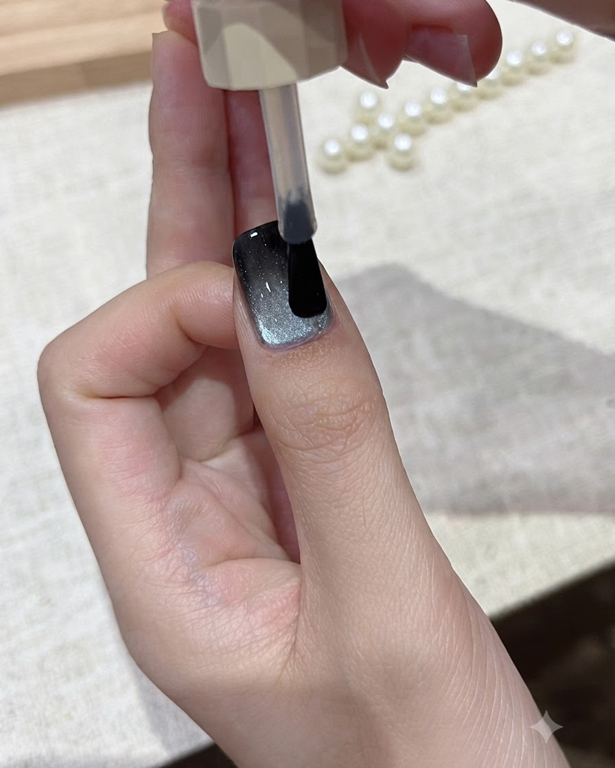 A brush gliding a layer of clear glossy top coat over the finished cat-eye nail design.