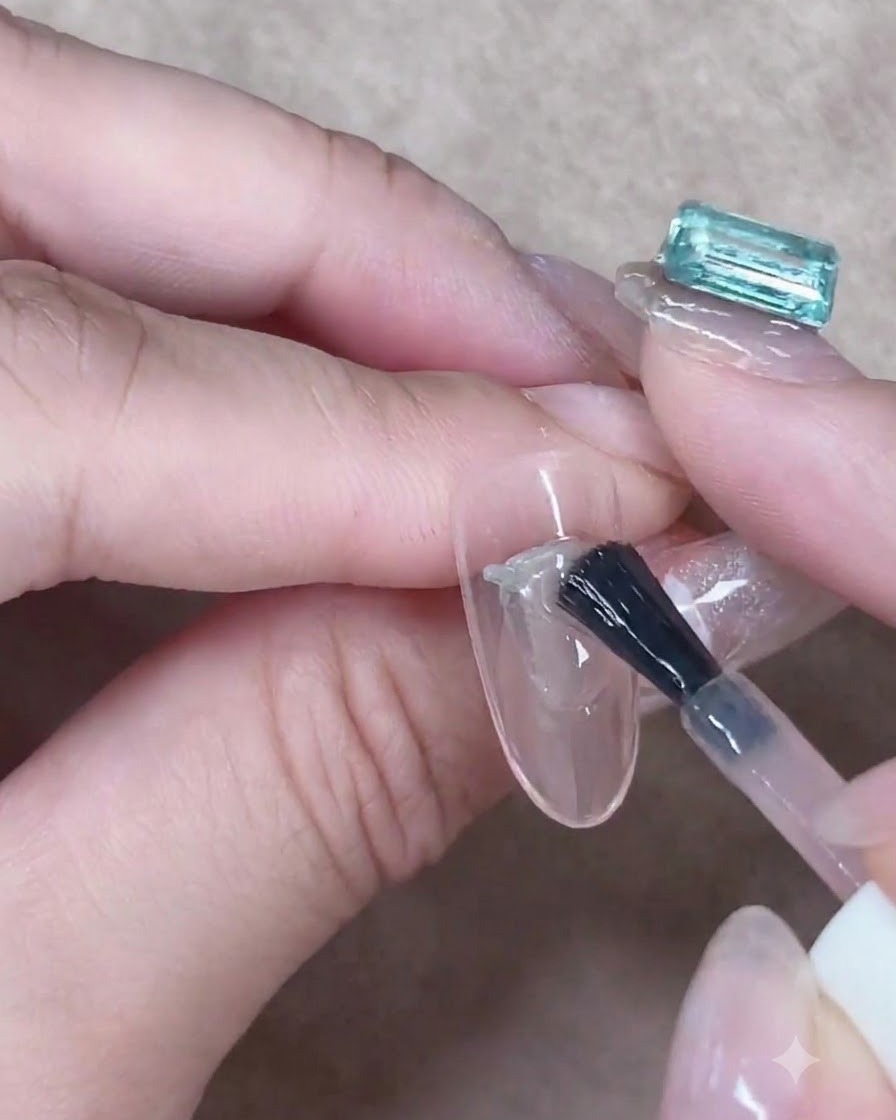A gel brush carefully smoothing a layer of translucent nude gel down the center of an almond-shaped nail.