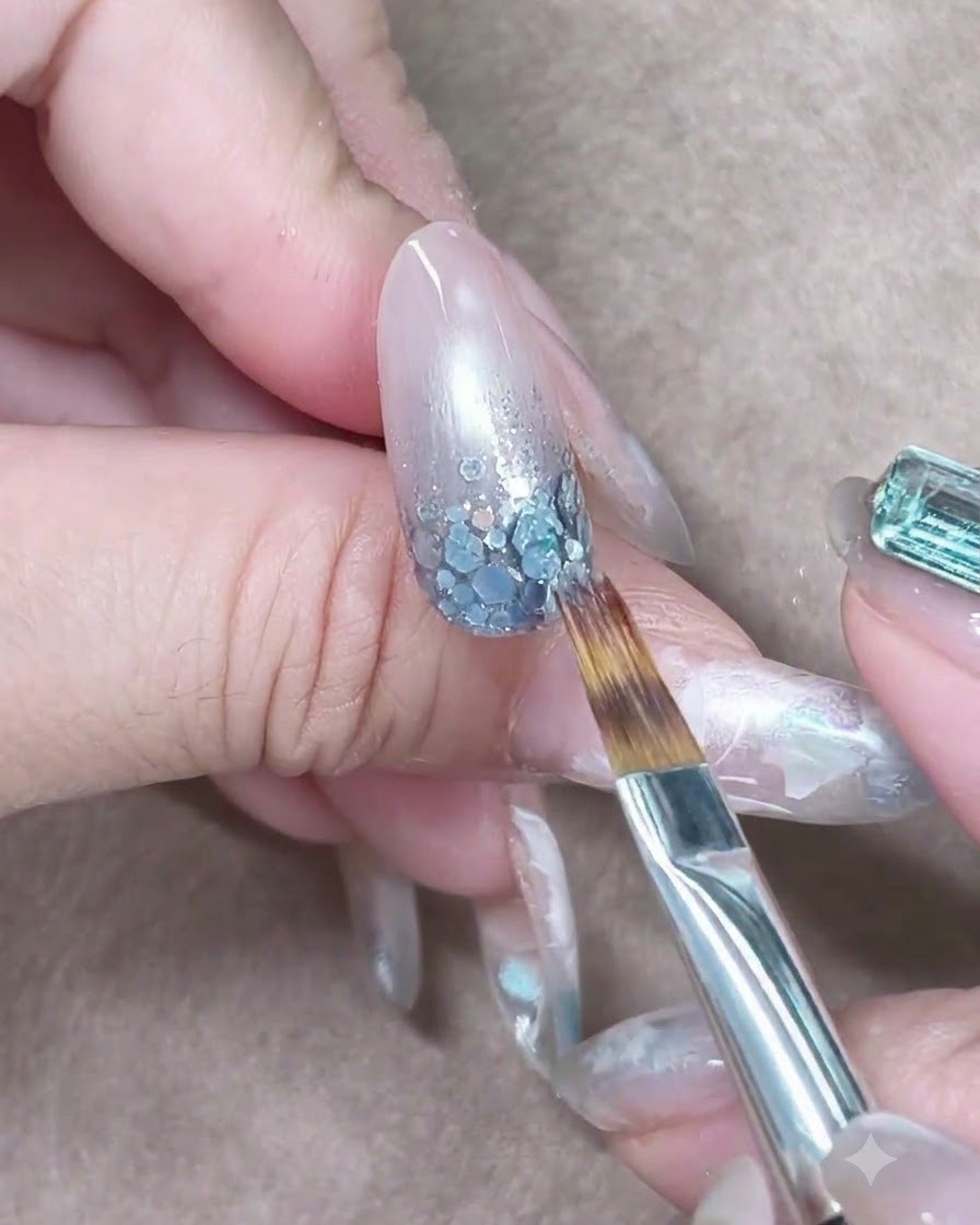 A brush lightly stroking translucent blue gel downward to blend the color gradient.
