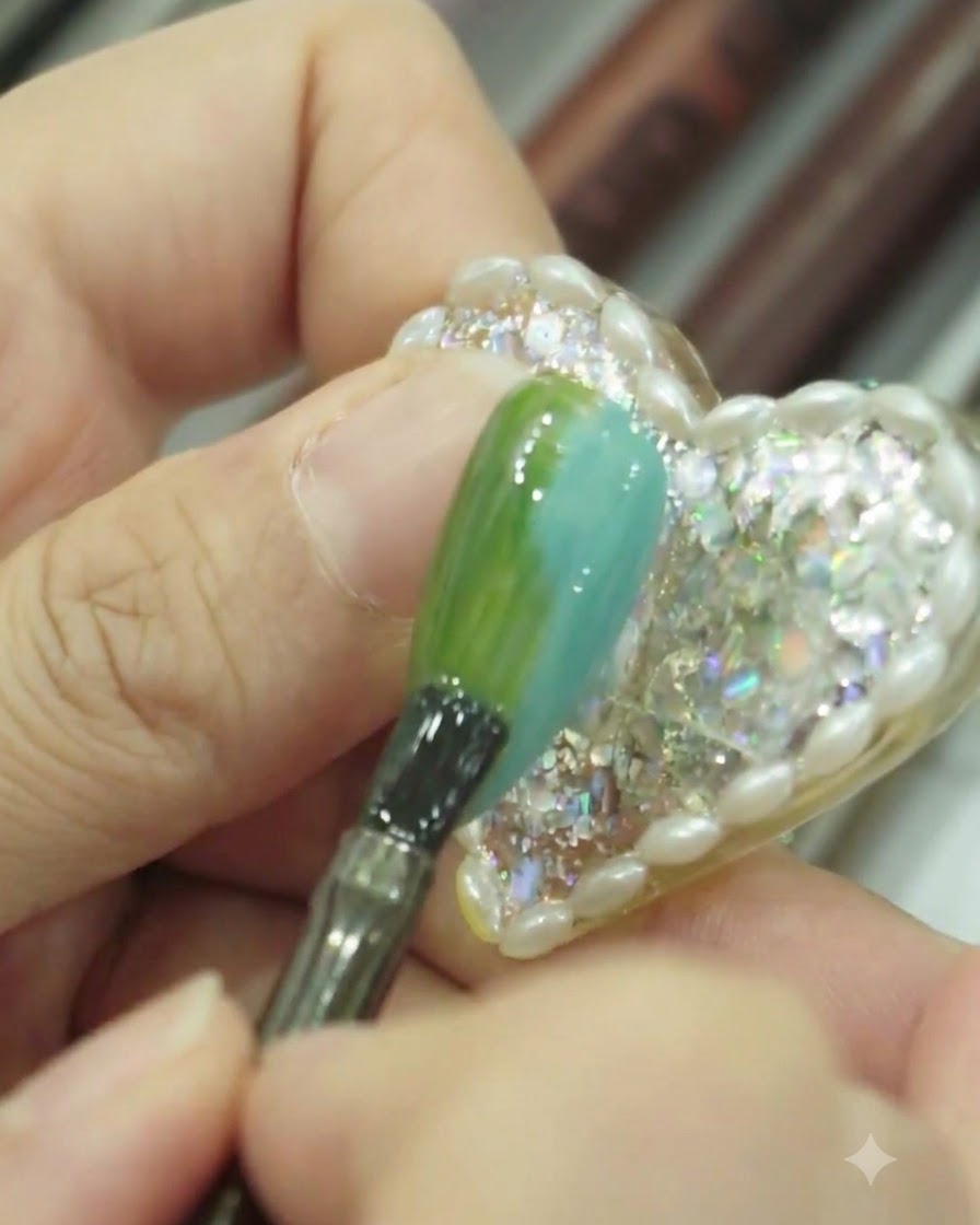 A close-up view of a brush lightly tapping and smoothing the surface of a blue and green gradient nail.