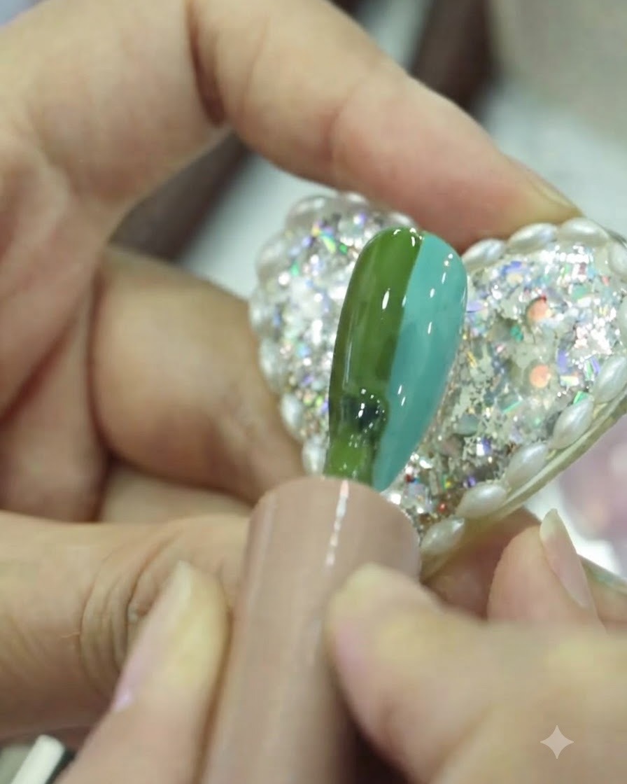 A flat brush softly blending the middle section where green and teal gel meet on the nail.