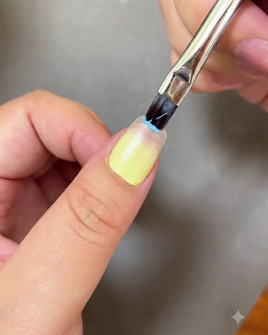 A nail brush applying light blue gel to the tip of a fingernail.