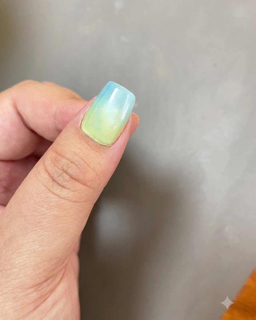 A fingernail with a blue-to-yellow ombre base and a circular cat eye magnetic light effect positioned under a purple UV/LED curing lamp.