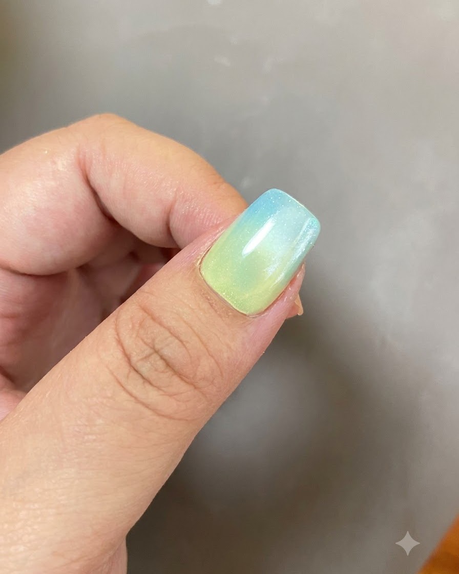 A completed gel manicure with a blue-and-yellow gradient and a glowing ring design under soft lighting.