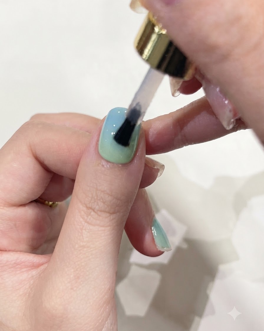 A brush applying clear builder gel over a gradient-colored fingernail.