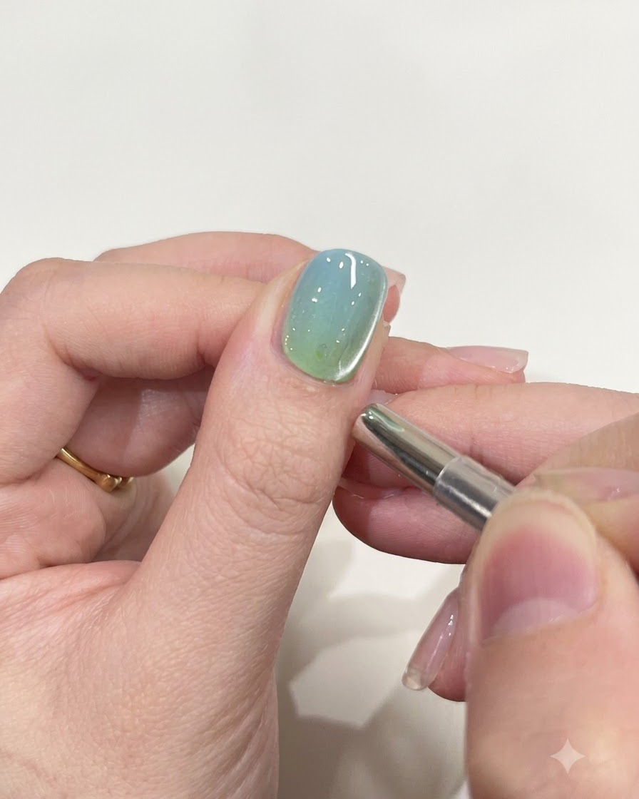 A small cylindrical magnetic tool hovering near the edge of a glossy gel-painted nail.