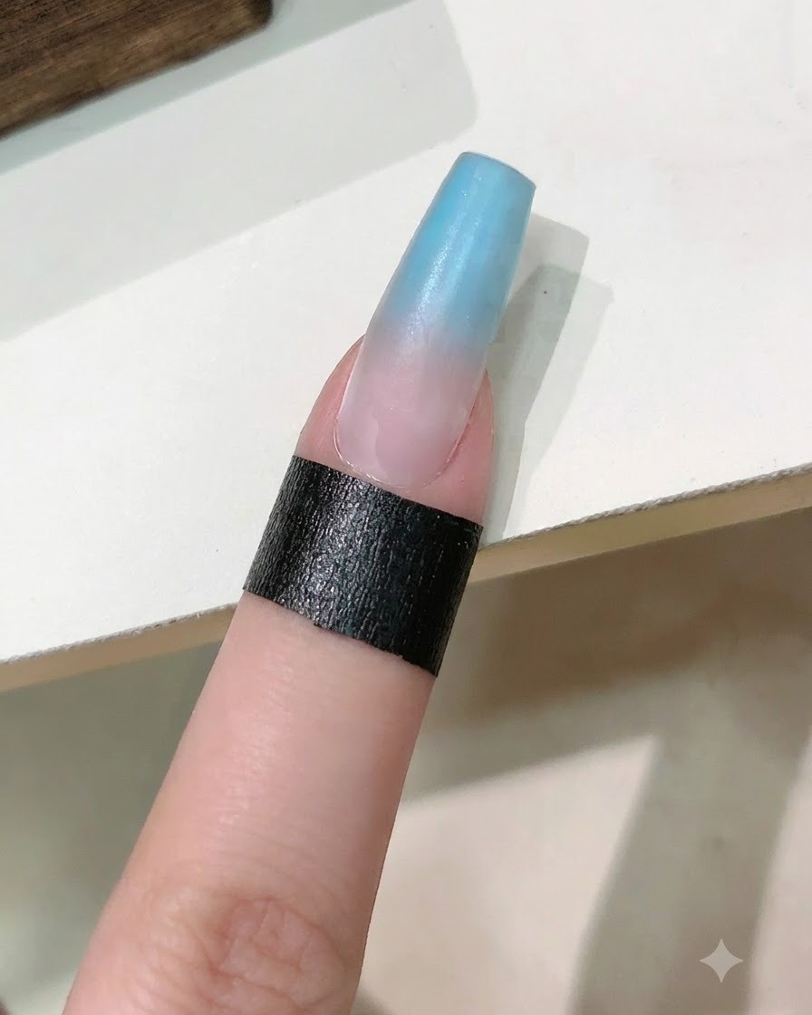 A nail brush applying a clear reinforcing gel coat over the blue and pink gradient nail.