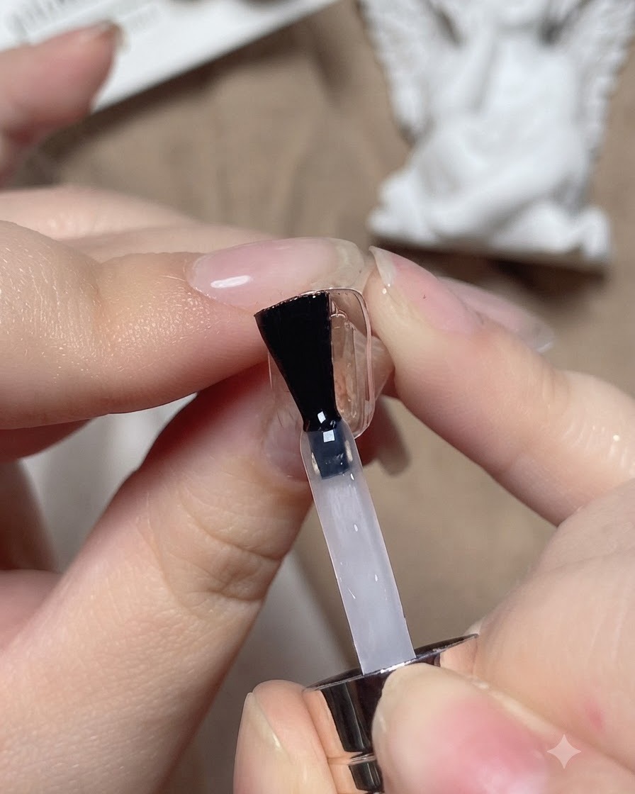 A nail brush applying a clear base coat onto a practice nail plate.