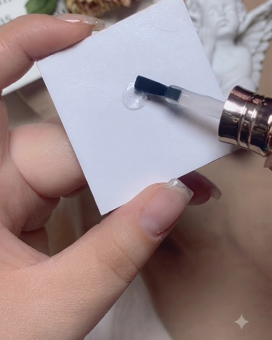A brush working a drop of base coat back and forth on a white palette surface.