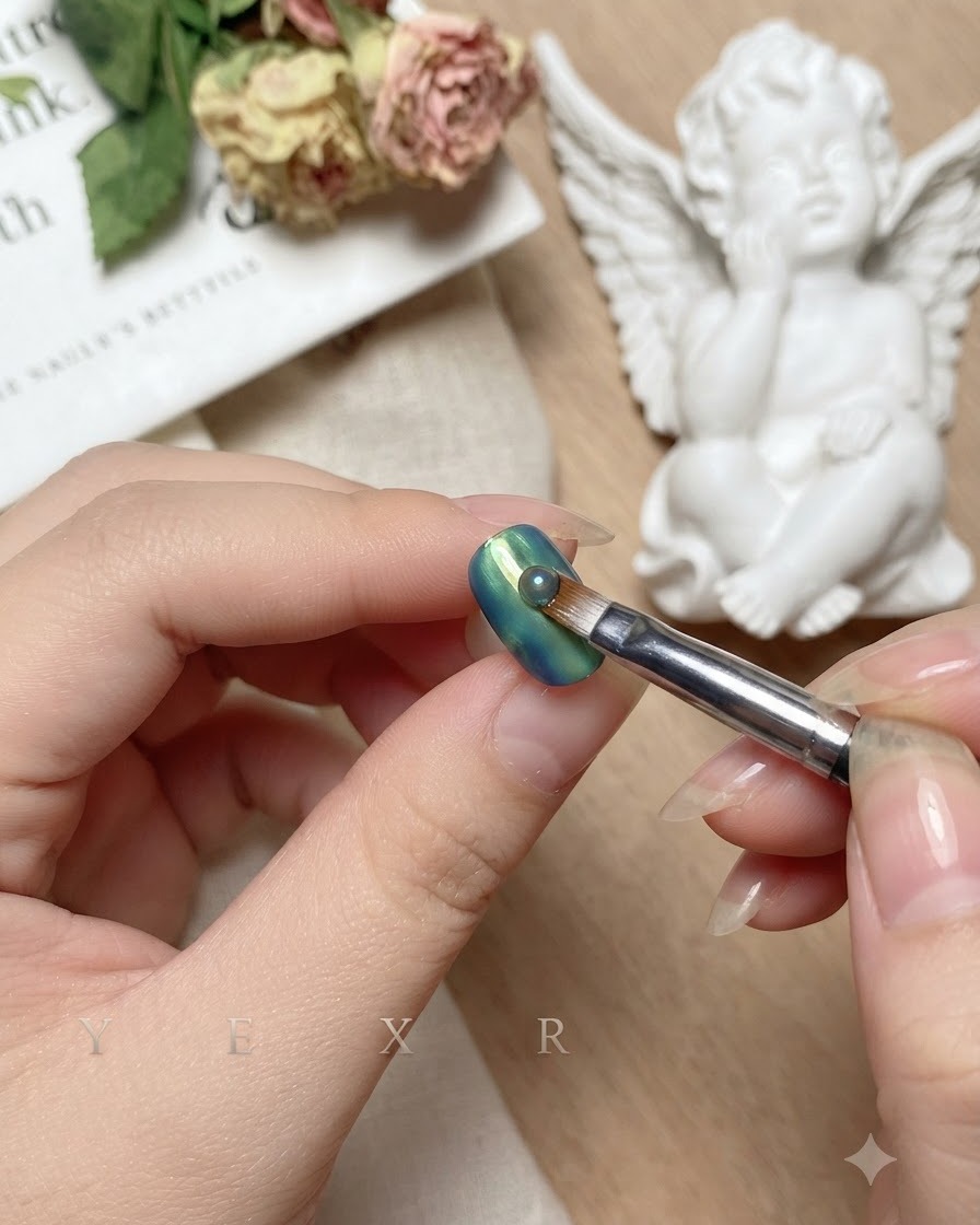 A brush pulling vertically down the center of the blended blue and green nail.