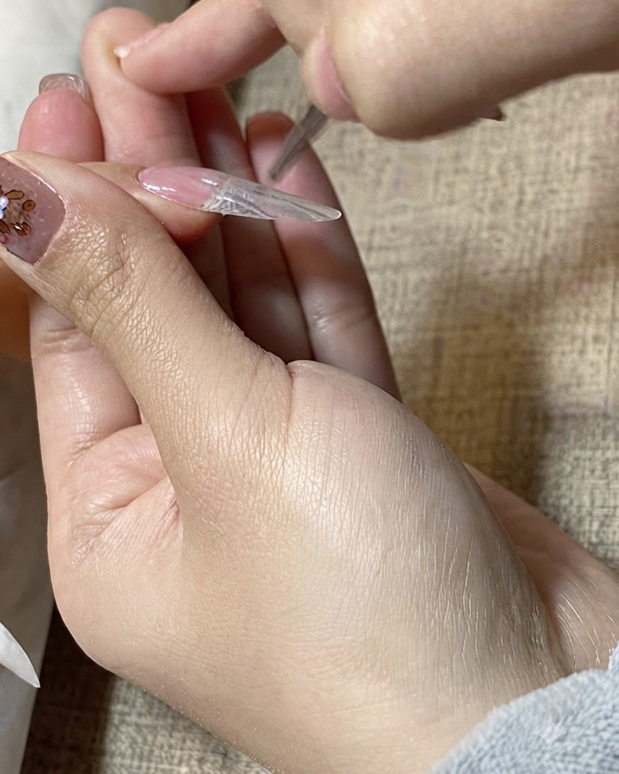 A close-up of a detailing brush smoothing clear gel over the surface of a nail extension.