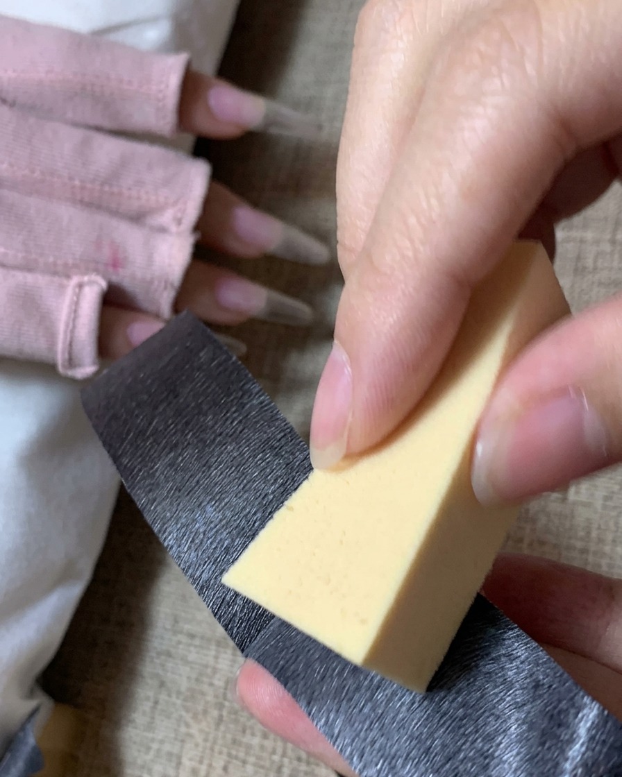 A person using black adhesive tape to clean dust off a triangular yellow makeup application sponge.