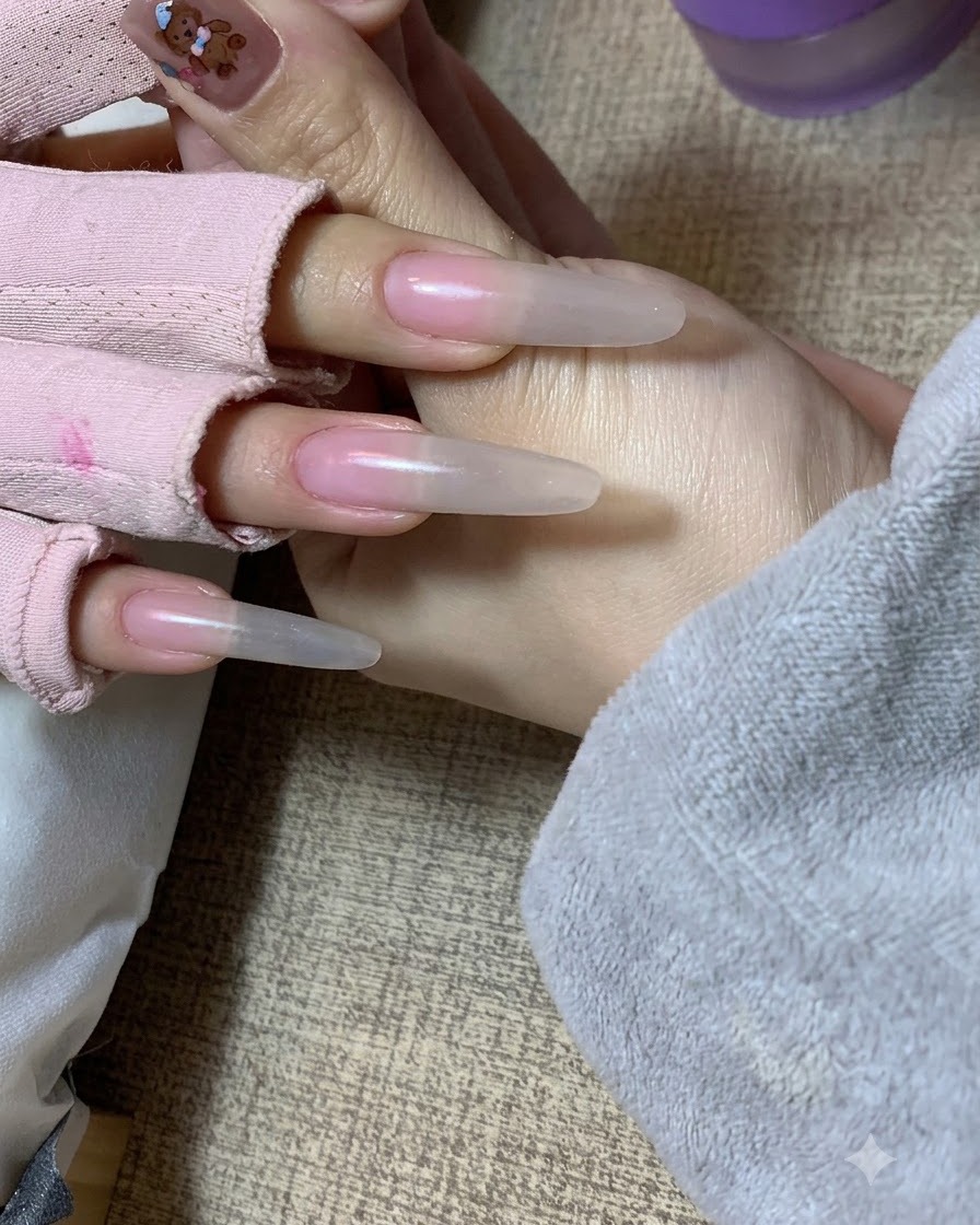 A hand holding a clients hand showing a soft nude gradient effect applied with a sponge on the nail extensions.