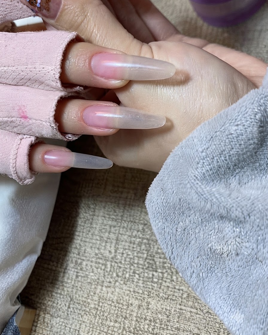 A close-up view of a hand receiving the second layer of nude gel patted carefully onto the free edge.