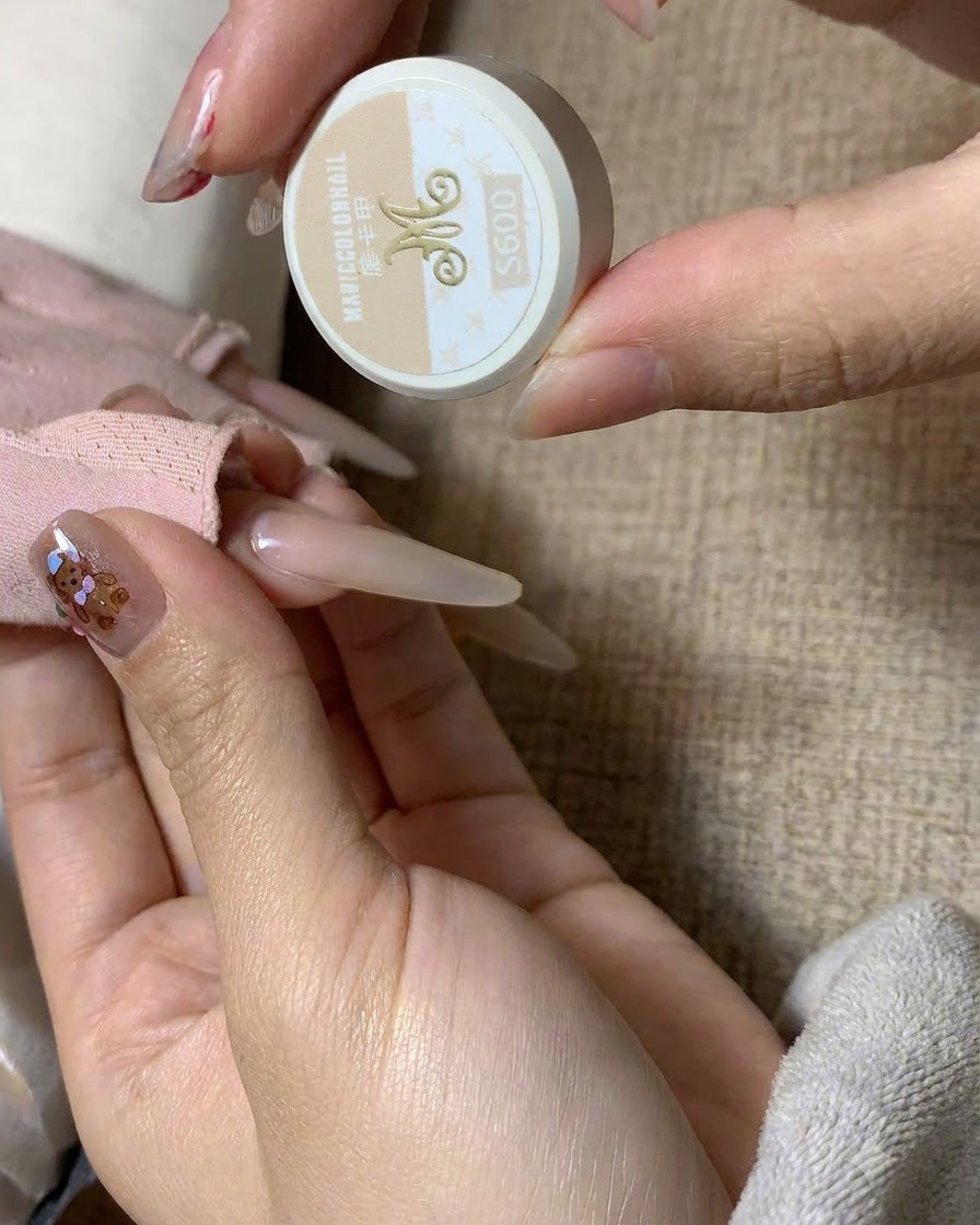 A close-up view of a fine brush dipping into a jar of MC Mocha milk tea color gel.